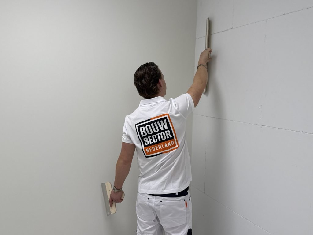 Stukadoor van Bouwsector Nederland trekt in de hoek van een kamer met een lange spaan een nieuwe wand recht